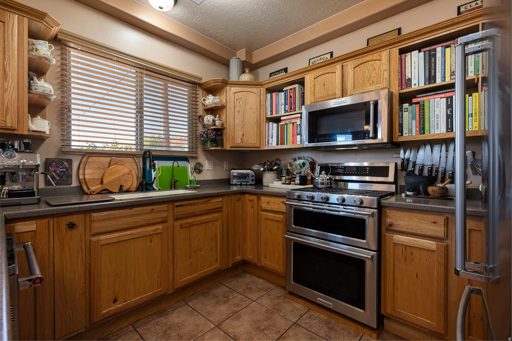Kitchen with open shelves, stainless steel appliances, dark countertops, a textured ceiling, and dark tile patterned floors