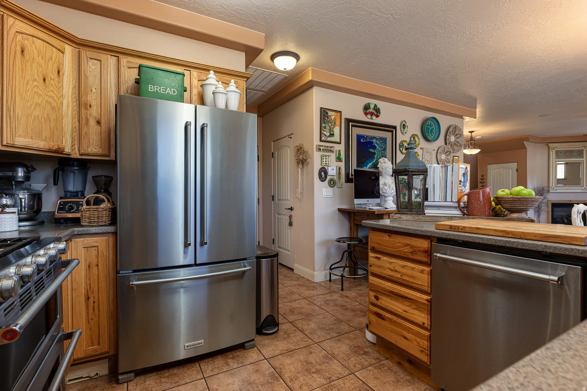 Kitchen featuring stainless steel appliances, light tile patterned floors, wood finish cabinetry, a textured ceiling, and ornamental molding