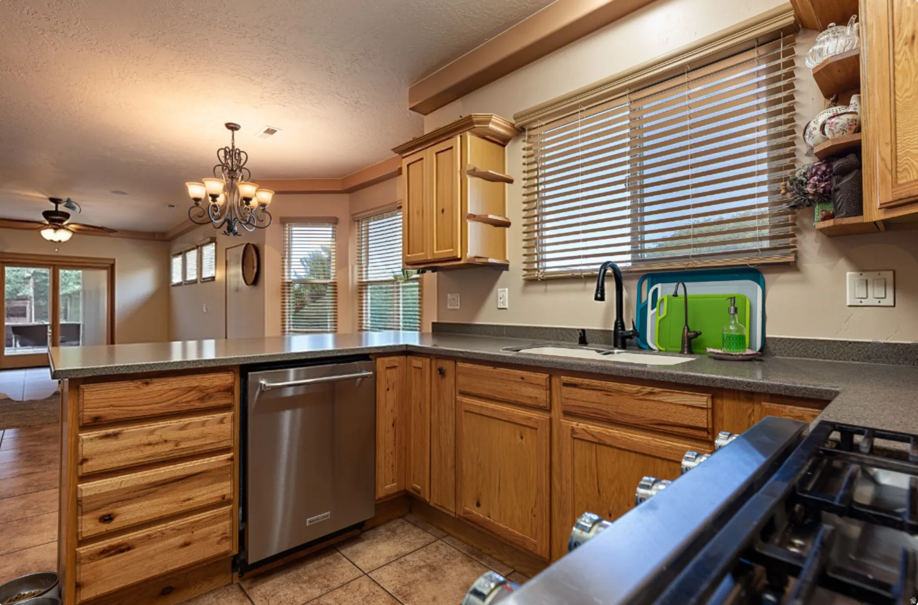 Kitchen featuring open shelves, stainless steel dishwasher, dark countertops, a peninsula, and ceiling fan