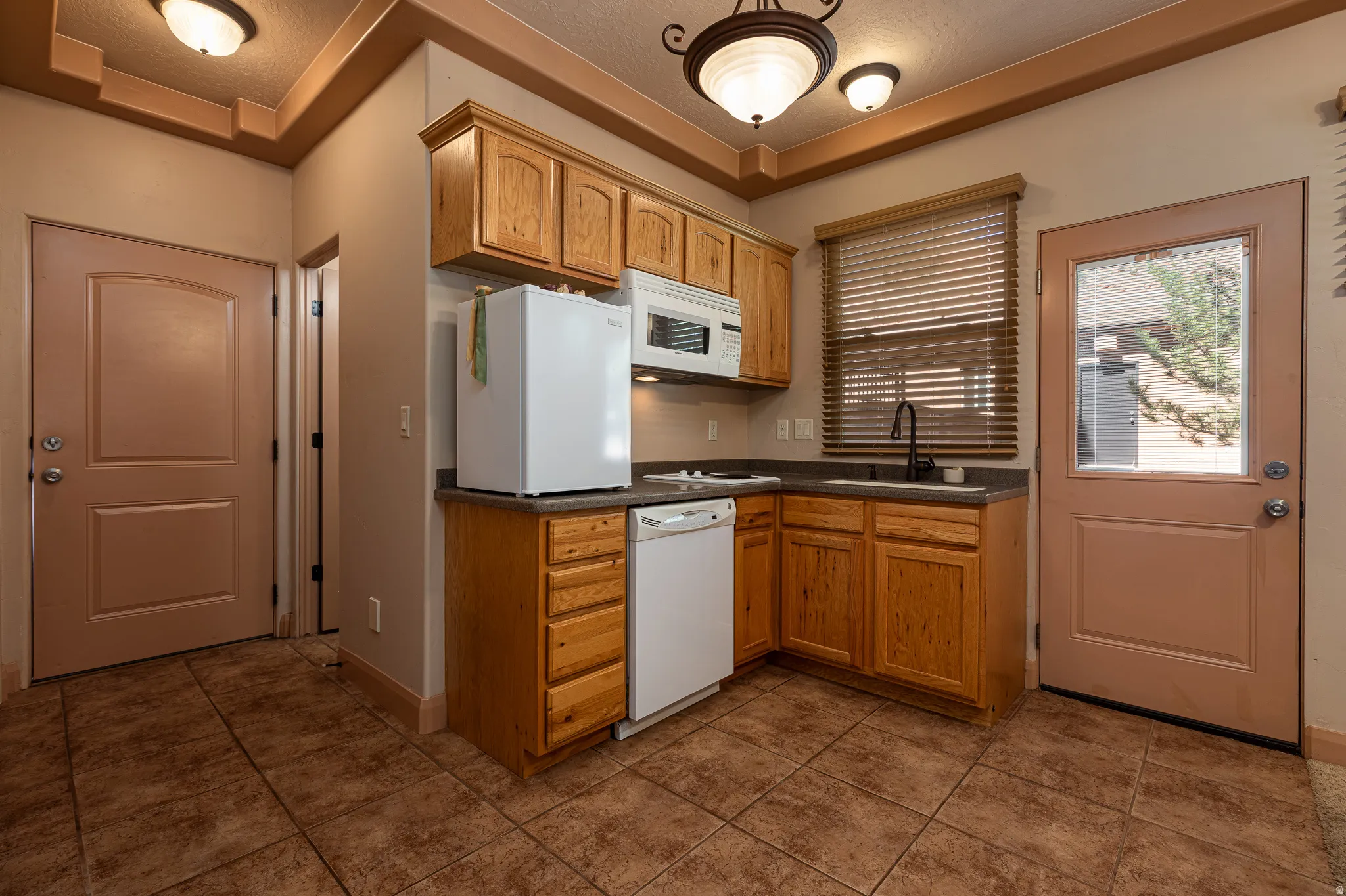 Kitchen featuring dark countertops, white appliances, a textured ceiling, and dark tile patterned flooring