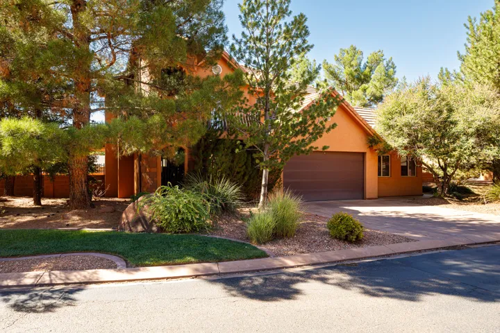 View of property hidden behind natural elements with driveway, an attached garage, stucco siding, and a tiled roof