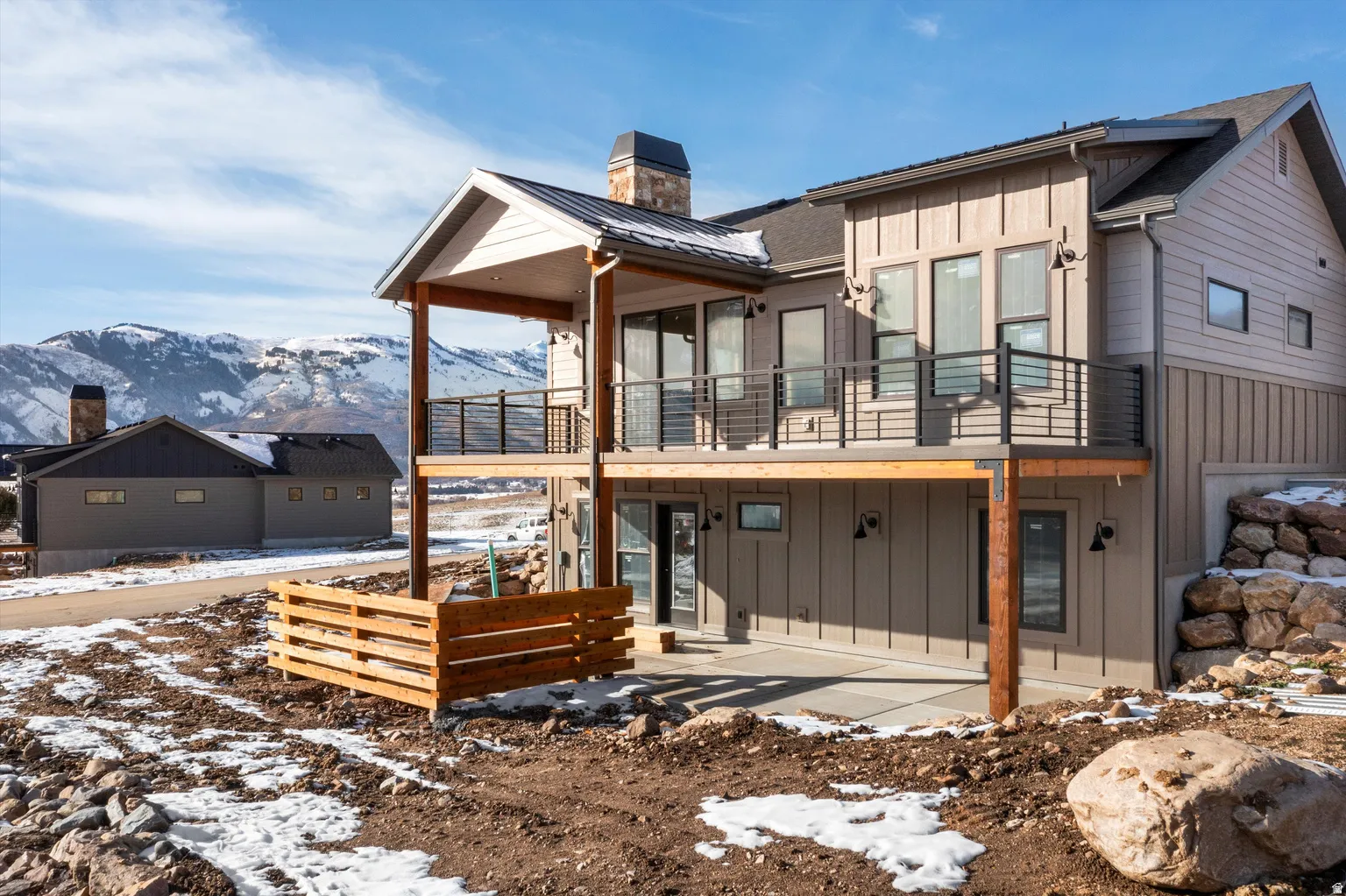 Snow covered back of property featuring board and batten siding, a patio, a deck with mountain view, and a chimney