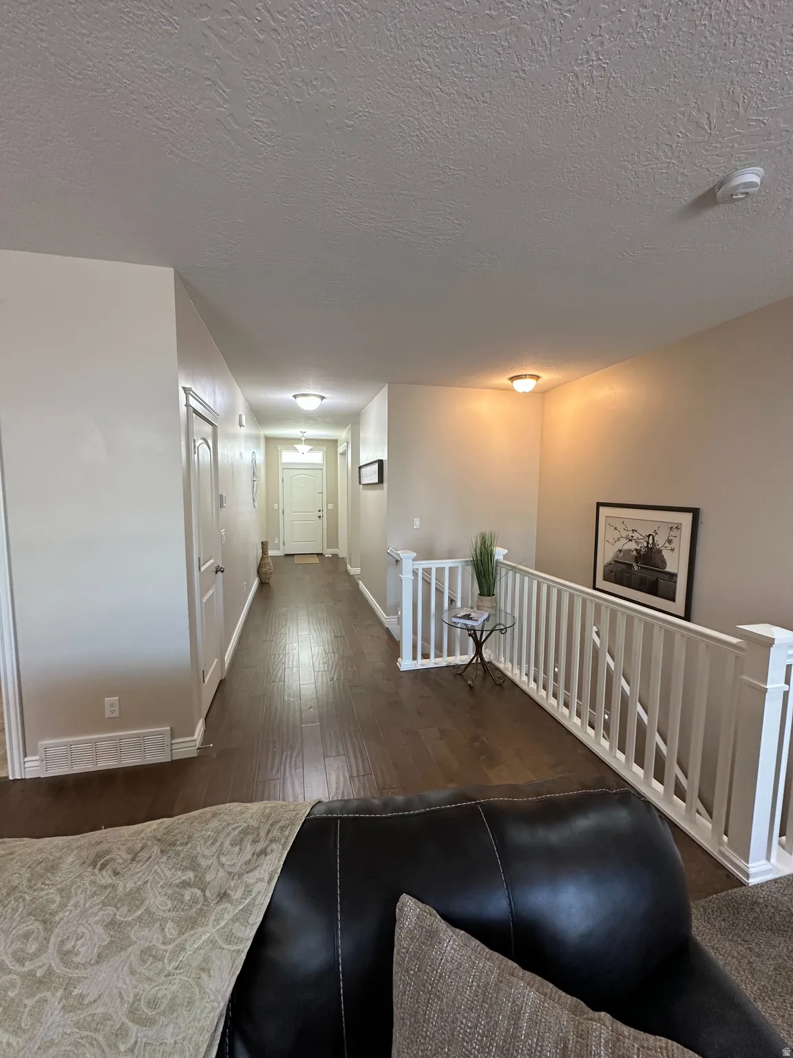 Corridor with dark wood-style flooring, an upstairs landing, and a textured ceiling