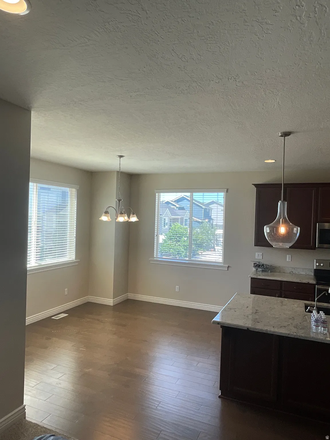 Unfurnished dining area featuring hanging lights, plenty of natural light, a textured ceiling, and dark wood-type flooring