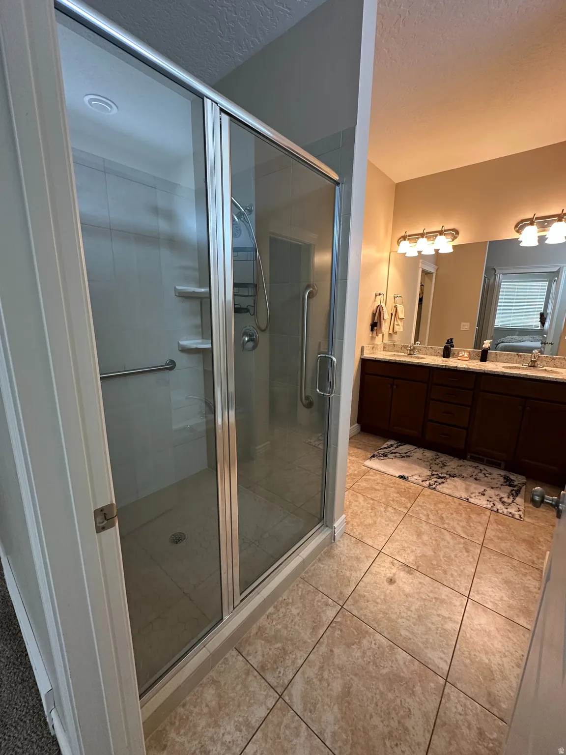 Bathroom featuring double vanity, a shower stall, a textured ceiling, and light tile patterned floors