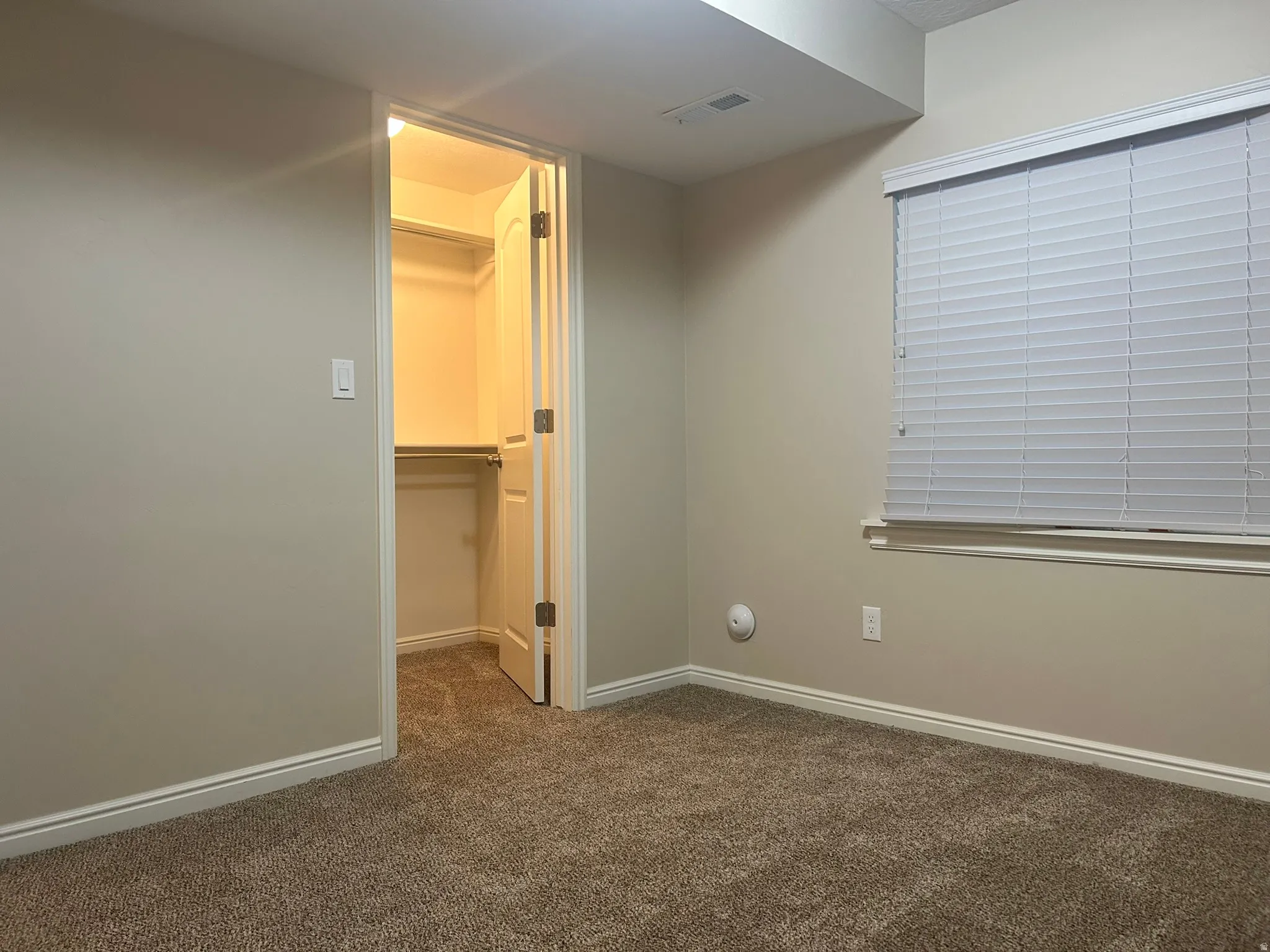 Unfurnished bedroom featuring a walk in closet and dark carpet