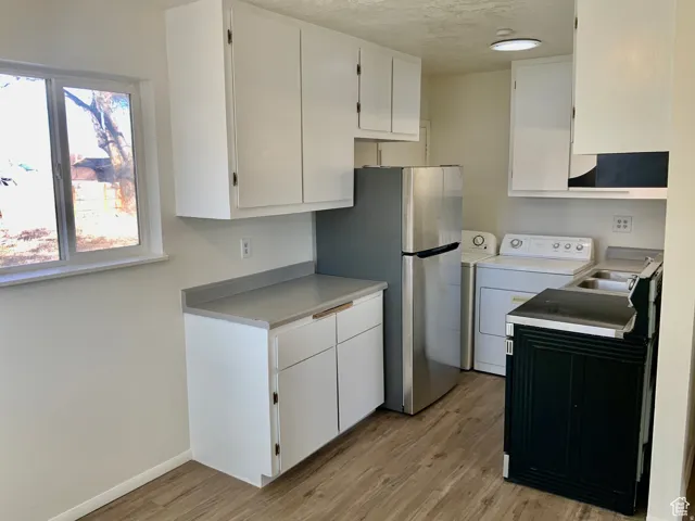 Kitchen with washer / dryer, white cabinets, freestanding refrigerator, light countertops, and light wood-style flooring