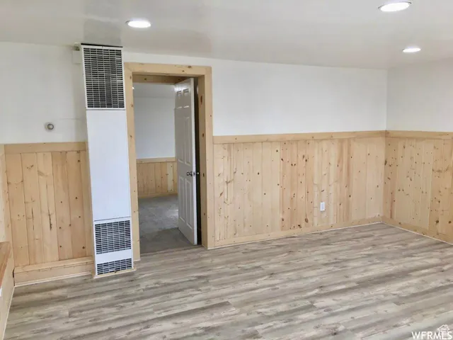 Spare room with wood walls, a wainscoted wall, a heating unit, and wood finished floors