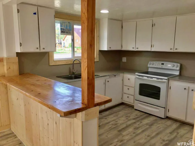 Kitchen featuring white electric range, wood counters, light wood-style flooring, a peninsula, and white cabinets