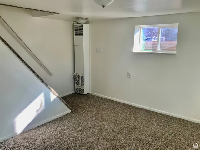Unfurnished room with dark colored carpet and a heating unit