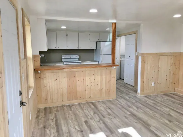 Kitchen with wooden walls, light wood-style flooring, white appliances, a peninsula, and wainscoting