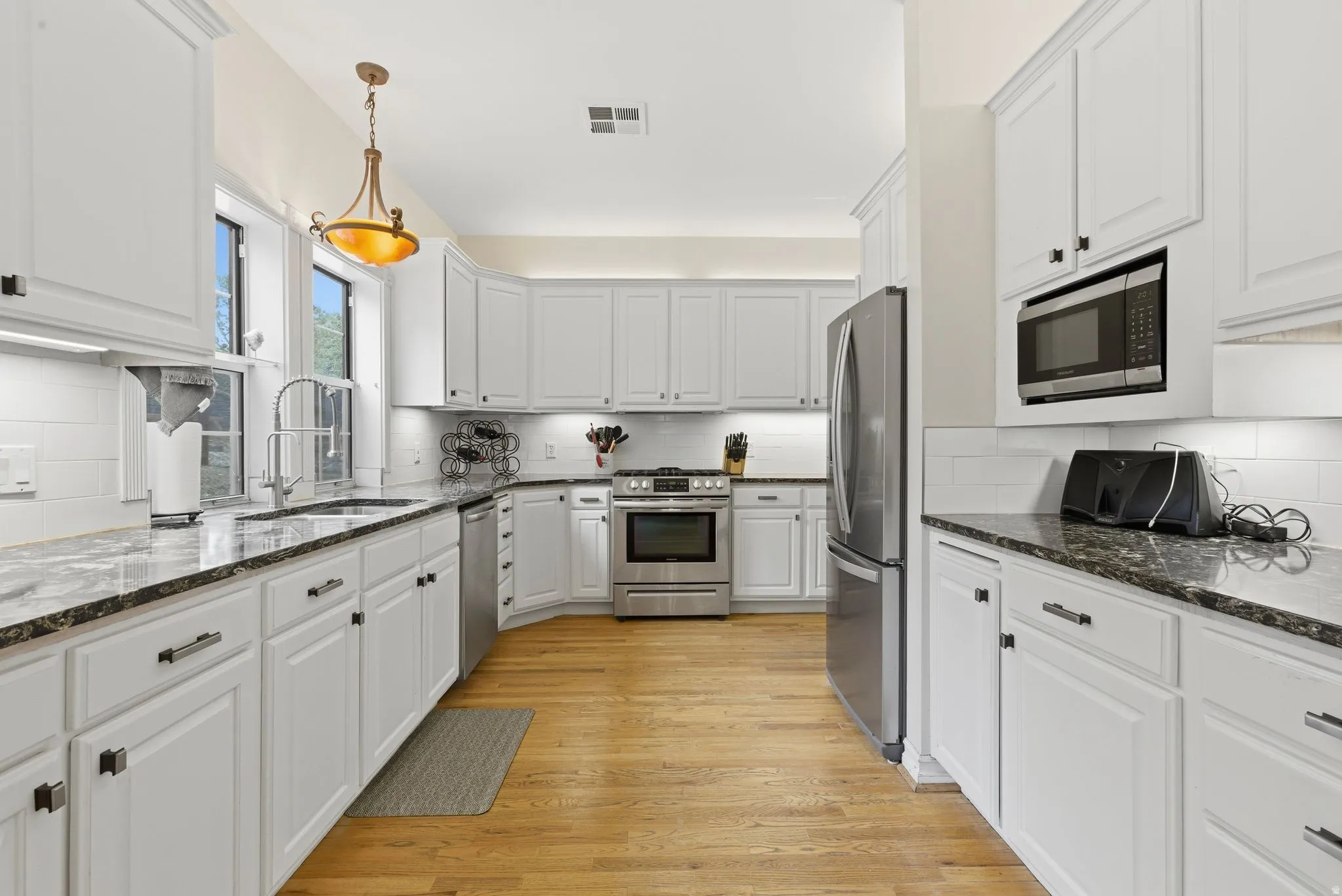Kitchen featuring dark stone counters, white cabinetry, tasteful backsplash, stainless steel appliances, and light wood finished floors