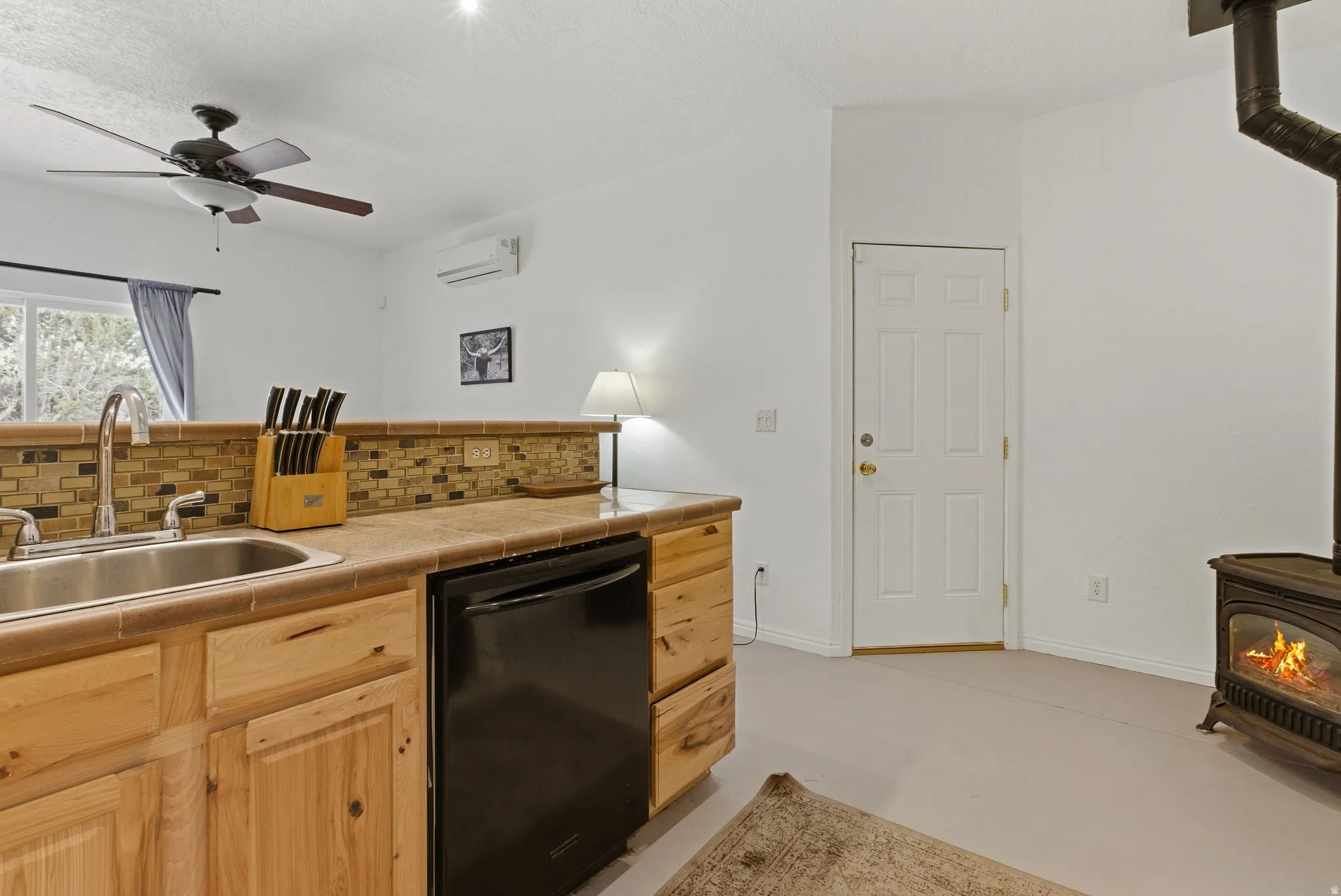 Kitchen with a wood stove, dishwasher, tasteful backsplash, a ceiling fan, and light wood finish cabinets
