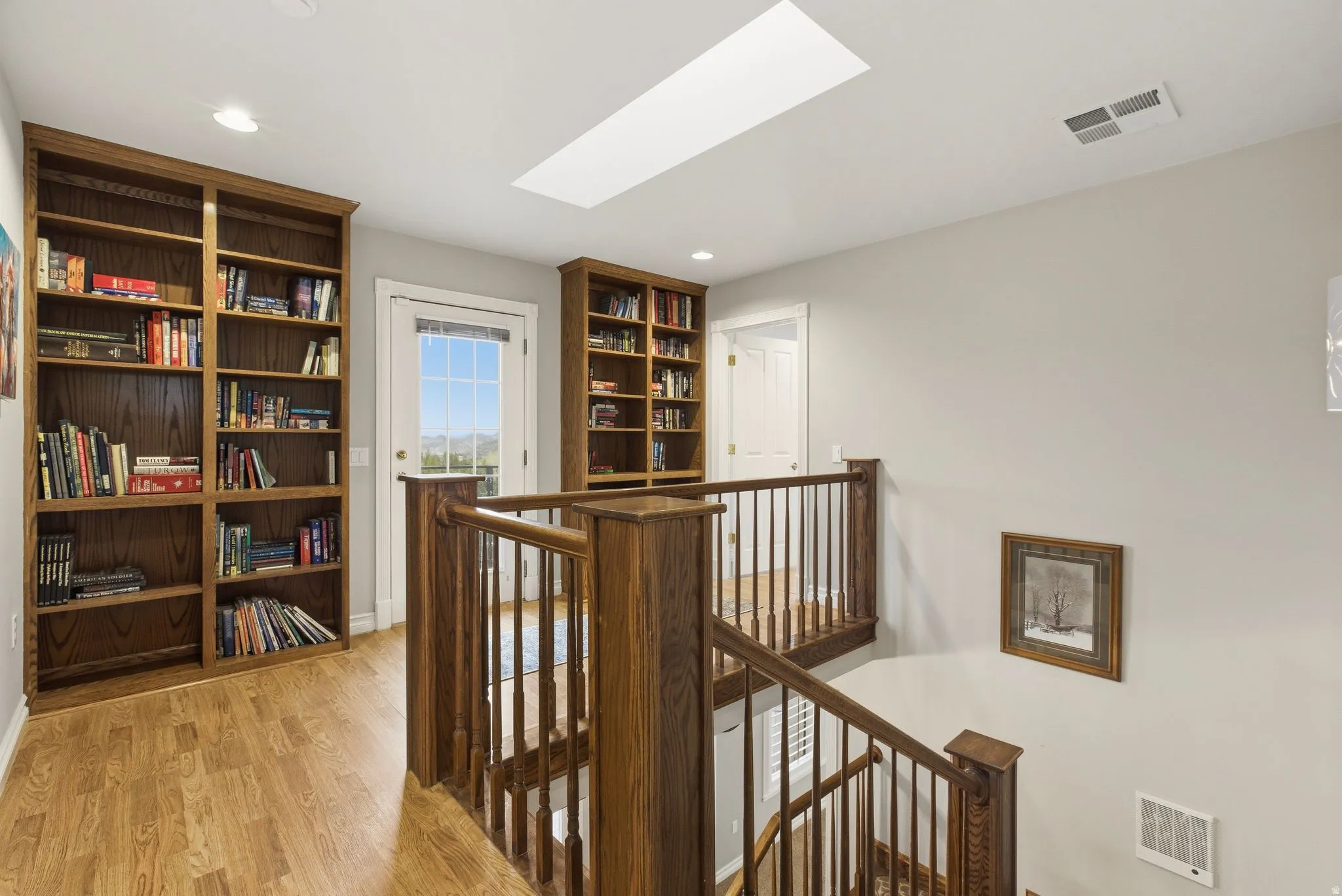 Corridor with an upstairs landing, a skylight, light wood-style floors, and recessed lighting