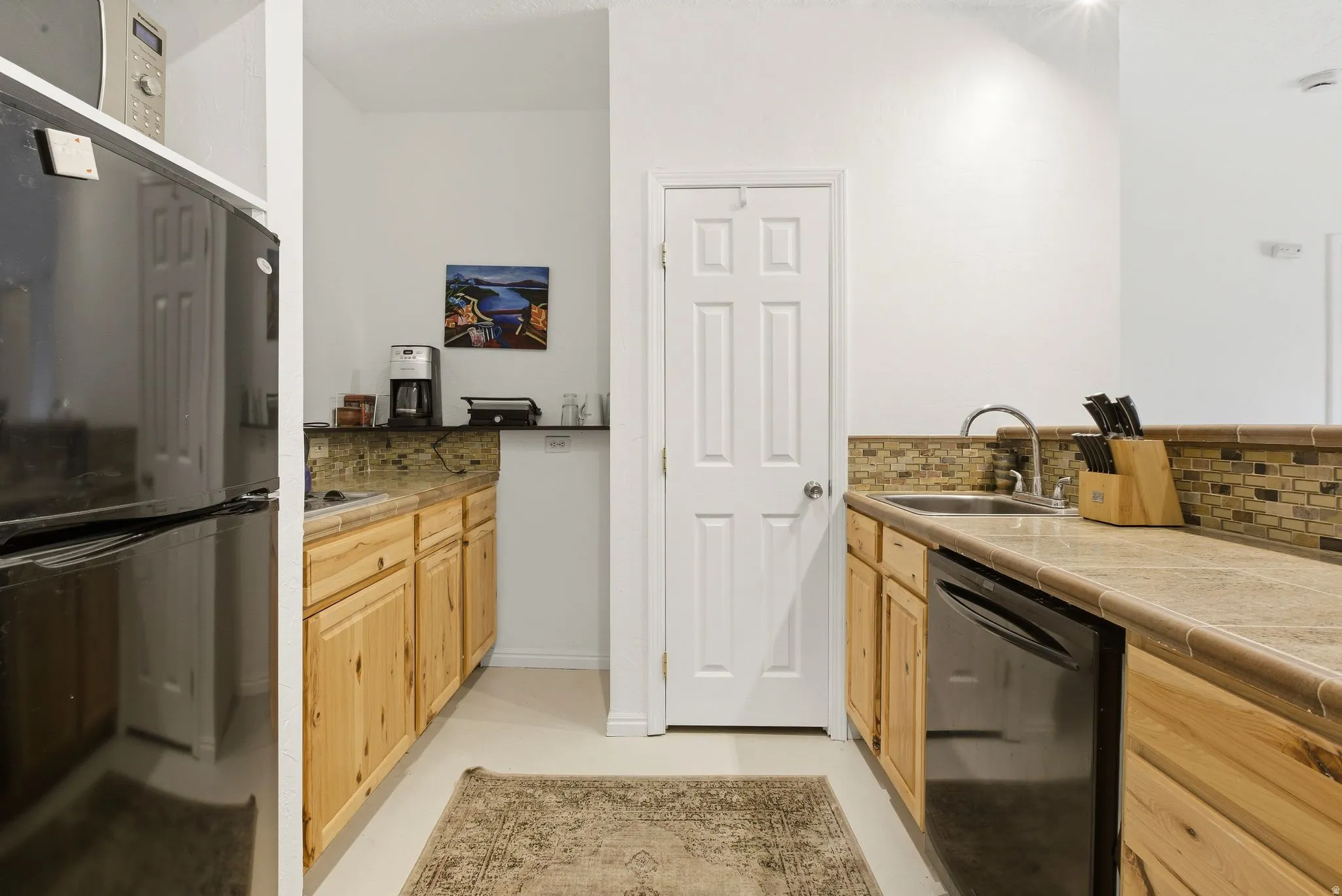 Kitchen with black appliances, light wood finish cabinets, tasteful backsplash, and tile countertops