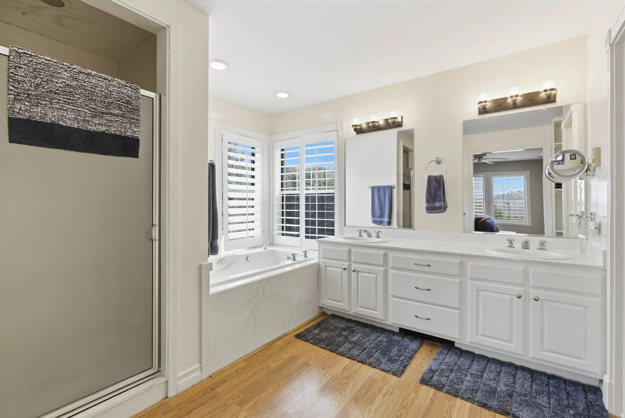 Full bathroom featuring a stall shower, double vanity, light wood-type flooring, ensuite bath, and a garden tub