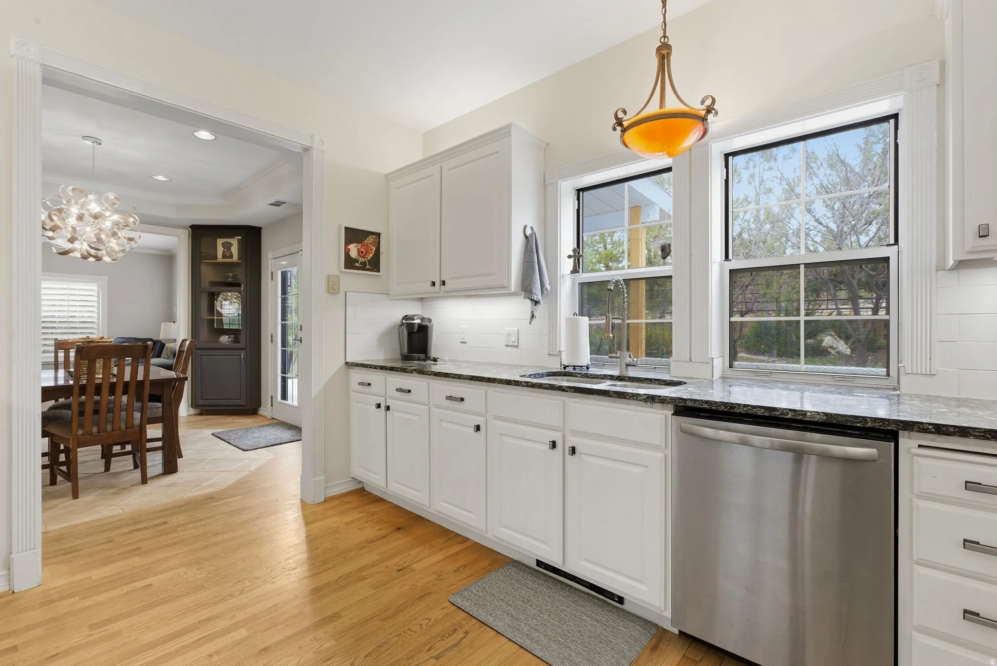 Kitchen with white cabinetry, dishwasher, dark stone countertops, backsplash, and light wood-style floors