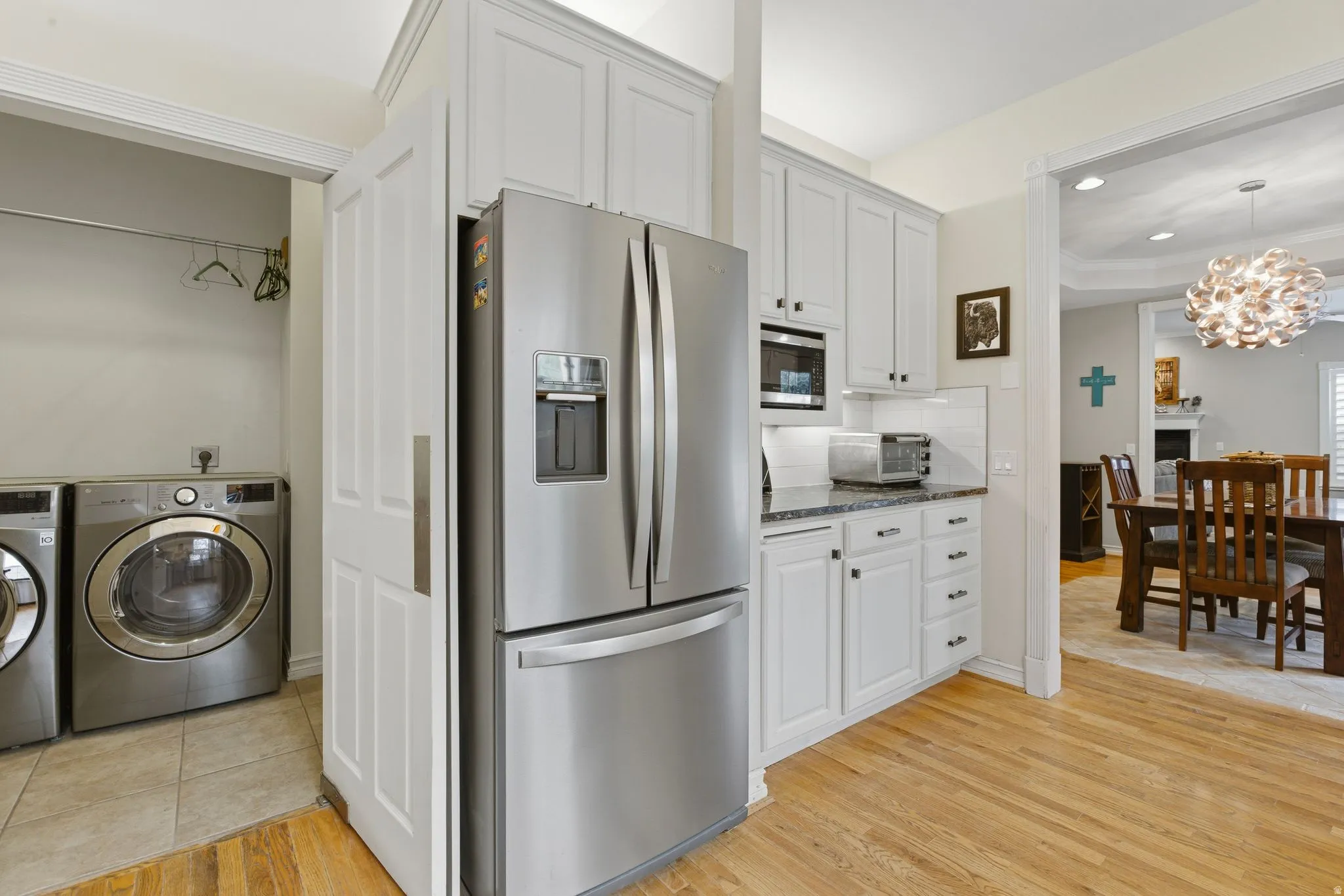 Kitchen featuring stainless steel appliances, hanging lights, dark stone countertops, light wood finished floors, and washing machine and dryer
