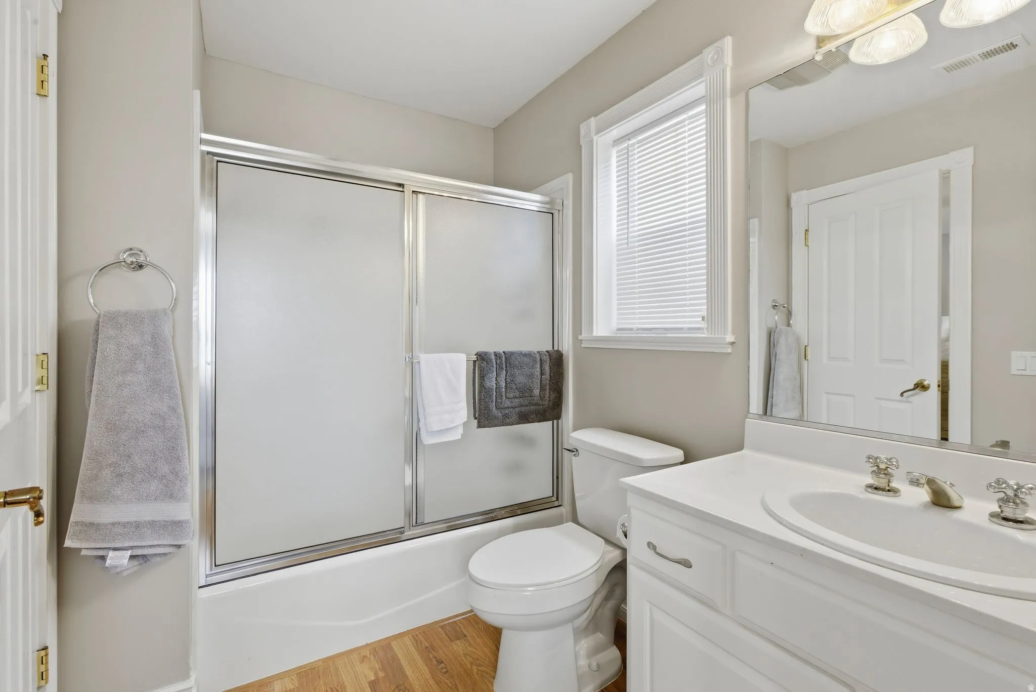 Full bath featuring bath / shower combo with glass door, vanity, and light wood-style flooring