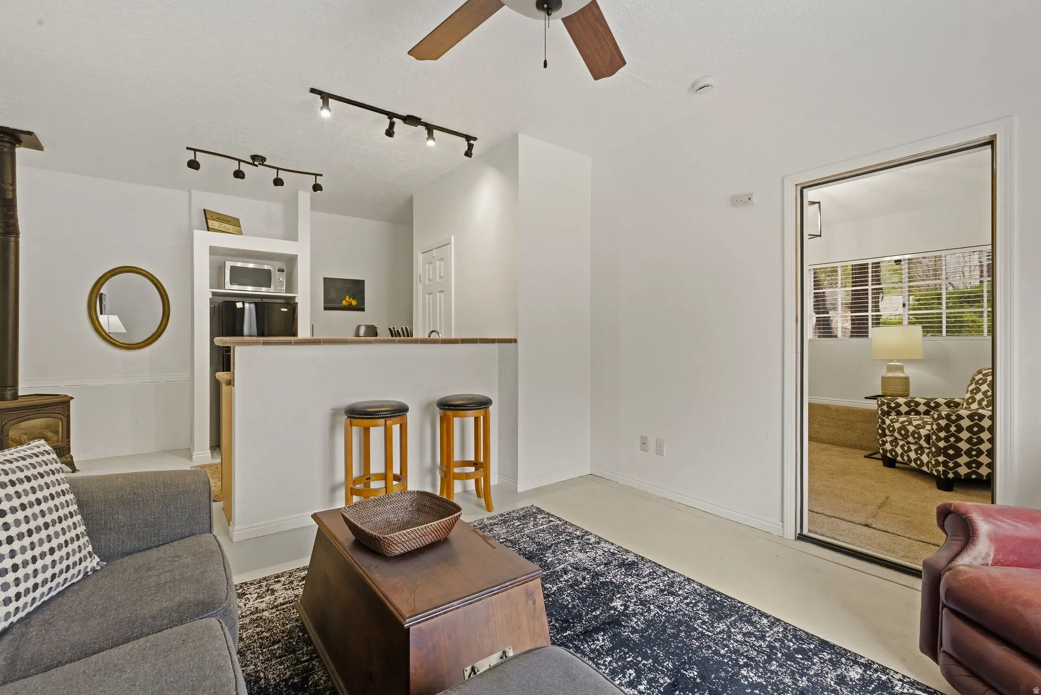 Living room with a ceiling fan, track lighting, finished concrete flooring, and a wood stove