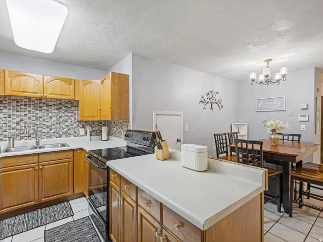 Kitchen with black / electric stove, light countertops, light tile patterned flooring, a textured ceiling, and suspended lighting
