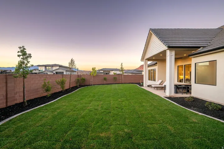 Expansive green lawn, covered patio, dark tile roof, exterior wall in a light tone, and a block perimeter wall