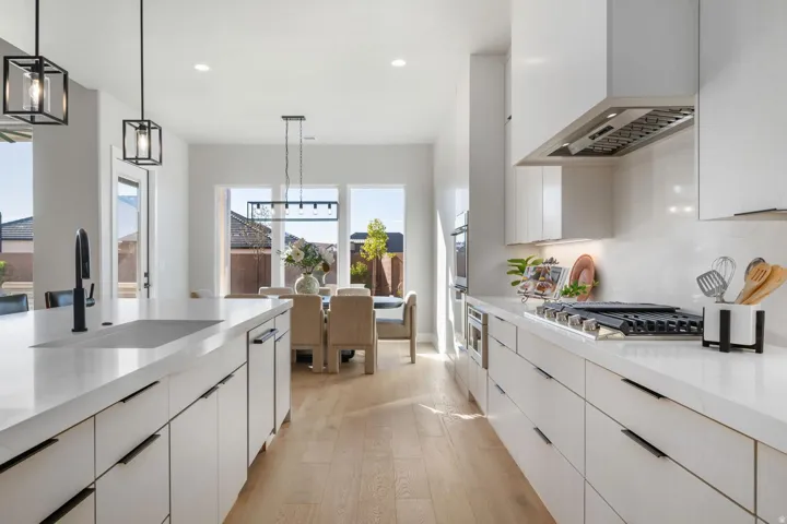 White cabinetry, light wood-finish flooring, stainless steel appliances, large kitchen island with integrated sink, and contemporary light fixtures
