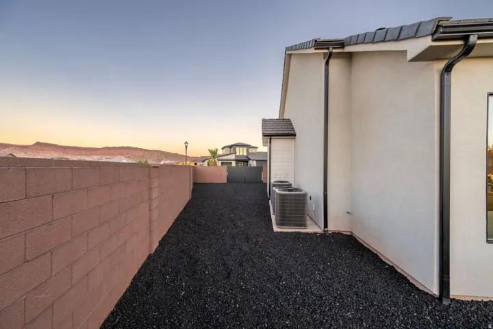 Exterior stucco siding with a tile roof, black gutters, and a gravel-covered ground