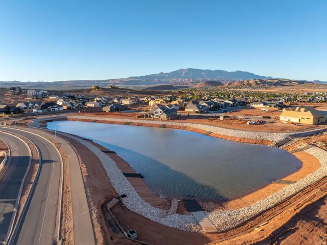 Man-made lake with a stone-lined bank, surrounding residential development, paved road, and distant mountains