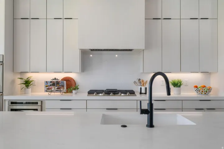Integrated kitchen featuring a gas range, built-in microwave, under-cabinet lighting, a large island with an undermount sink, and a black gooseneck faucet