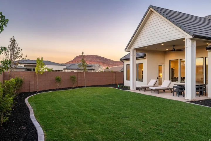Expansive backyard featuring a manicured lawn, concrete patio, and a covered outdoor living area with a ceiling fan