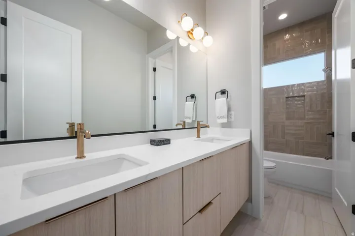 Dual vanity with integrated sinks, wood-finish cabinetry, gold-tone hardware, and a large mirror