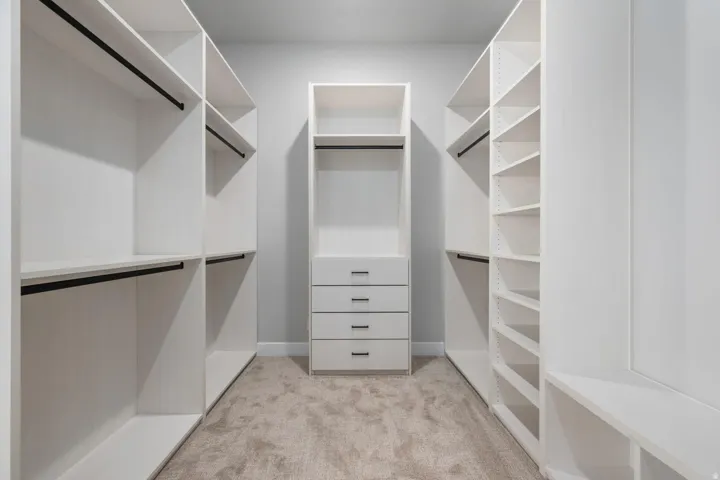 Walk-in closet featuring built-in white cabinetry, integrated shelving, hanging rods, and a four-drawer dresser