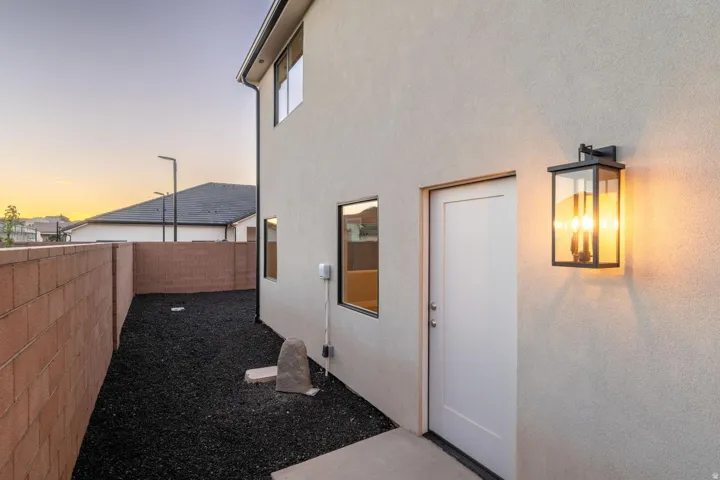 Stucco exterior with a decorative wall sconce, concrete block perimeter wall, and a side entry door