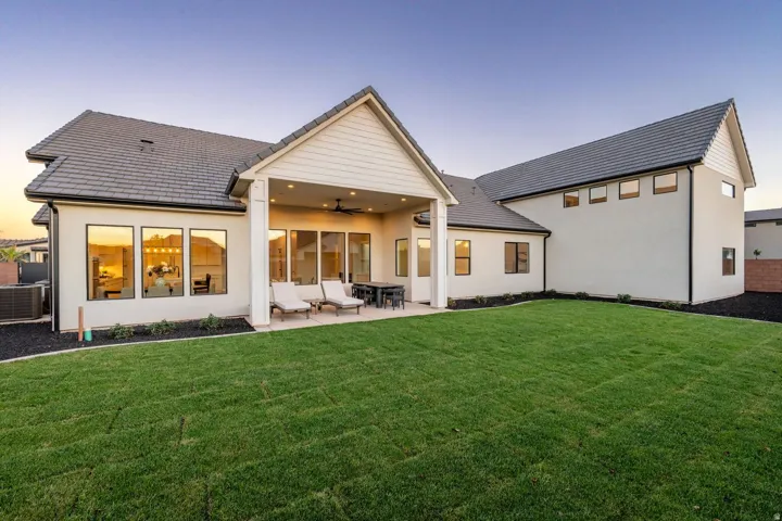 Expansive green lawn, covered patio with recessed lighting, large pane windows, and stucco exterior