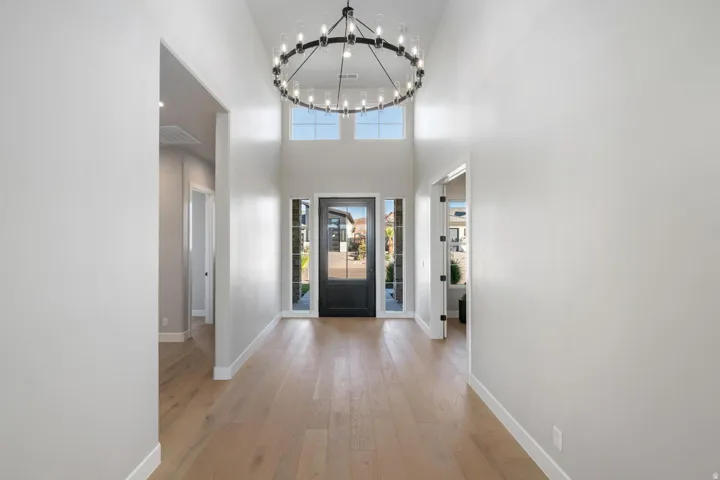 Double-height foyer with a circular chandelier, hardwood-finish flooring, and a dark-paneled front door with sidelights