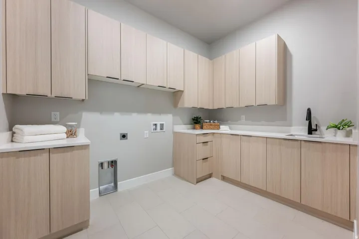 Extensive light wood-finish cabinetry, white countertops, built-in sink, matte black faucet, and light tile flooring