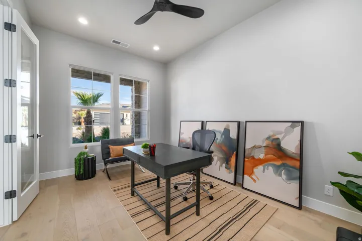 Modern home office featuring a black metal desk with lower shelving, light wood-finish flooring, and a striped area rug