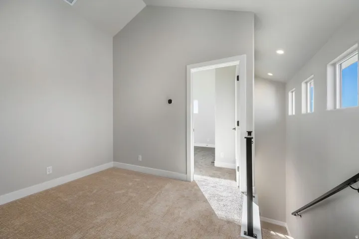 Carpeted flooring, vaulted ceiling, white trim, recessed lighting, and a black metal handrail