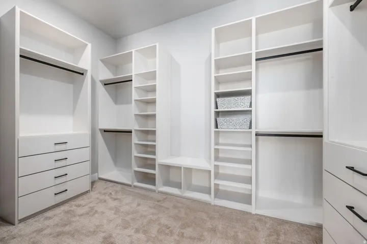Custom closet system featuring white cabinetry, multiple hanging rods, integrated shelving, and built-in drawers with black hardware