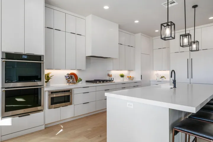 Spacious kitchen featuring white cabinetry, light-toned wood-finish flooring, stainless steel double ovens, a built-in microwave, and an oversized island with a matte black faucet