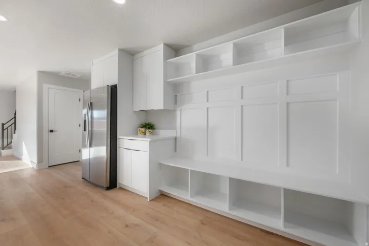 Built-in shelving with integrated bench seating, stainless steel refrigerator, white cabinetry, recessed lighting, and wood-finish flooring