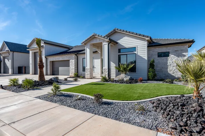 View of front facade with stone siding, a front lawn, an attached garage, concrete driveway, and a tile roof