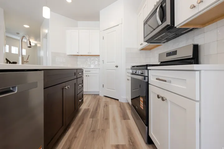 Modern kitchen featuring wood-finish flooring, white cabinetry, a built-in stainless steel microwave, and a stainless steel oven range