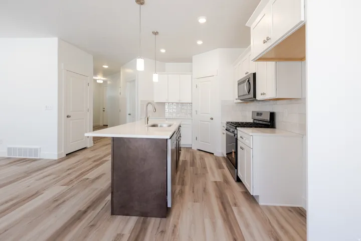 Modern kitchen featuring a central island with a sink, white cabinetry, stainless steel appliances, light-colored wood-finish flooring, and white subway tile backsplash