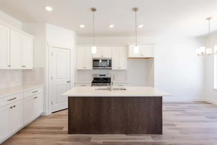 Kitchen featuring white cabinetry, a central island with a contrasting base and integrated sink, stainless steel appliances, and wood-finish flooring