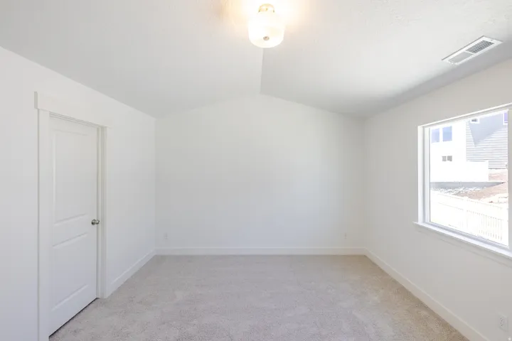 Room featuring vaulted ceilings, light-colored carpeting, white baseboards, a white paneled door with brushed nickel hardware, and a window with white trim