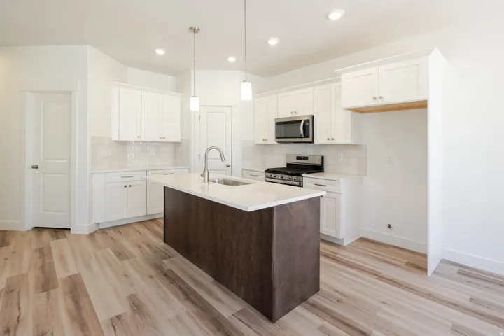Modern kitchen featuring a central island with a sink, white cabinetry, stainless steel appliances, a subway tile backsplash, and wood-finish flooring