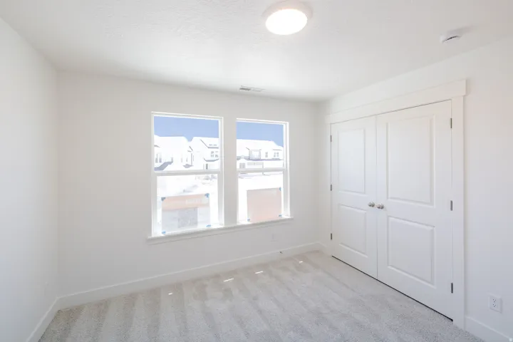 Light-filled interior space featuring two windows, neutral carpeting, white walls, and a double-door closet with satin nickel hardware