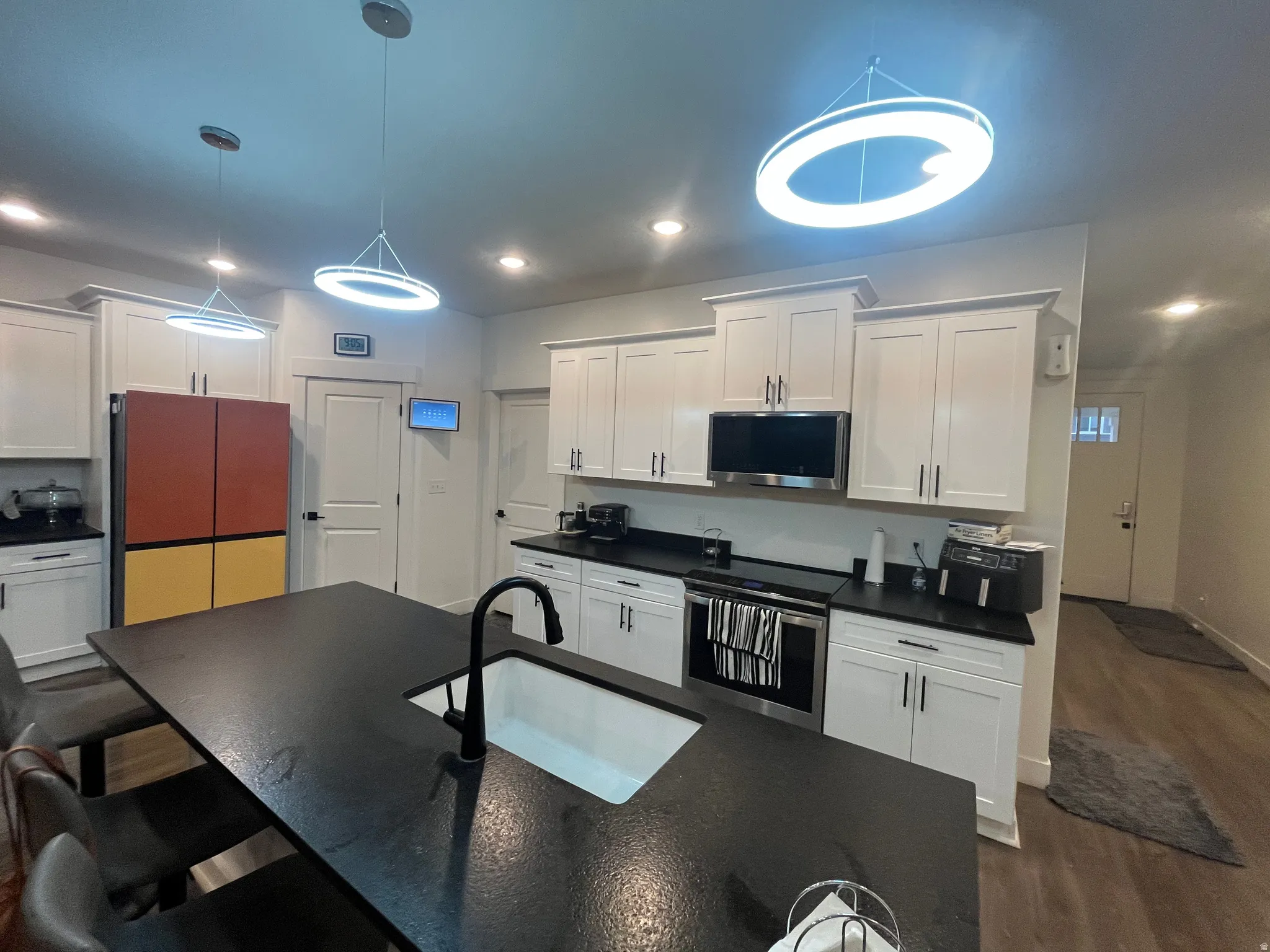 Kitchen with stainless steel appliances, white cabinetry, hanging light fixtures, and dark wood-style flooring